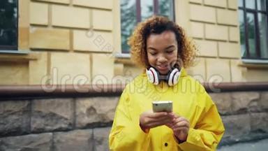 快乐的非裔美国学生正在使用智能手机浏览或短信朋友站在户外的现代街道上